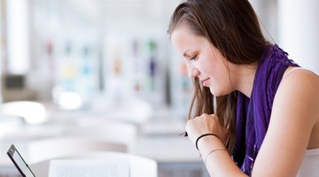 A female college student reads a book next to her laptop