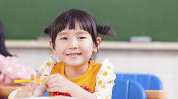 A girl reading a book in a classroom at her desk.