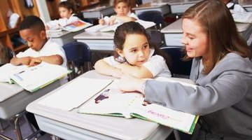 Teacher talking to young student at desk.
