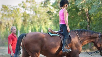 A man is teaching a young girl how to ride.