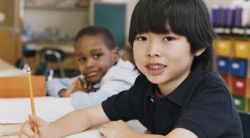 Two young school children are sitting in class writing.