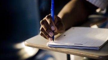 Close-up of student's hand writing in notebook at desk